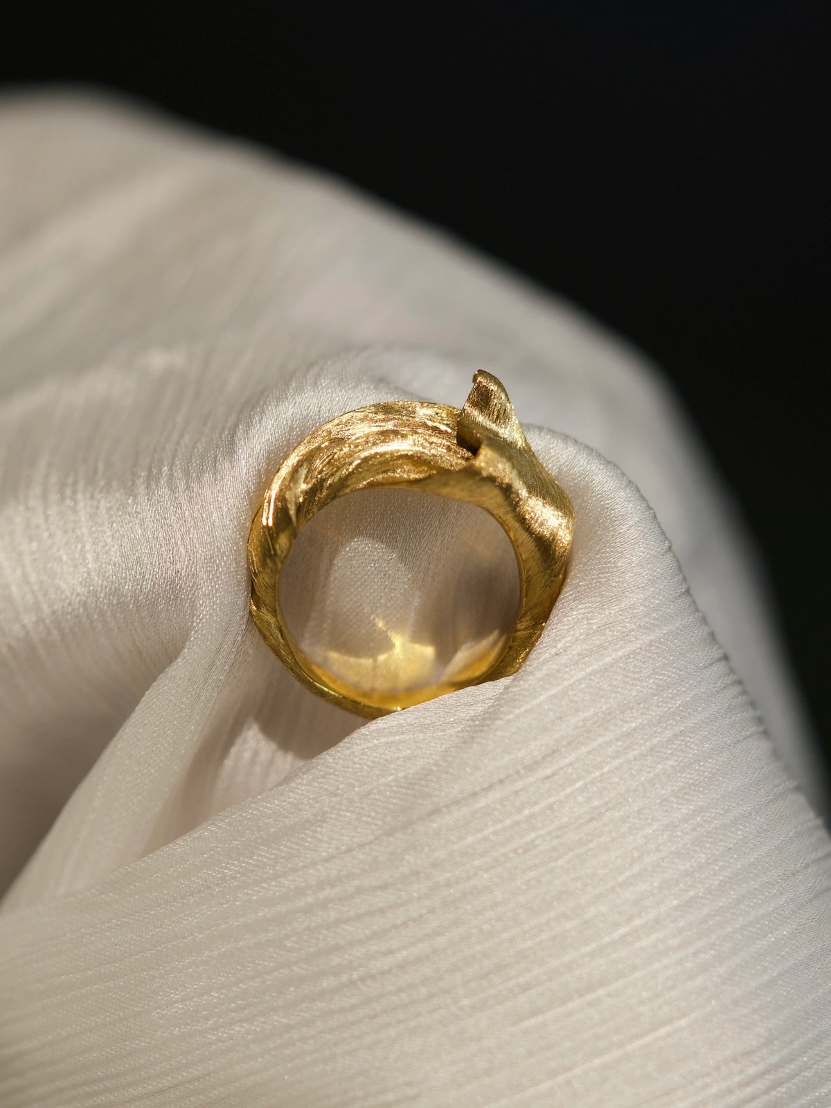 Front view of the Silk in Gold ring on folded pale fabric, showing its circular opening and raised gold fold.