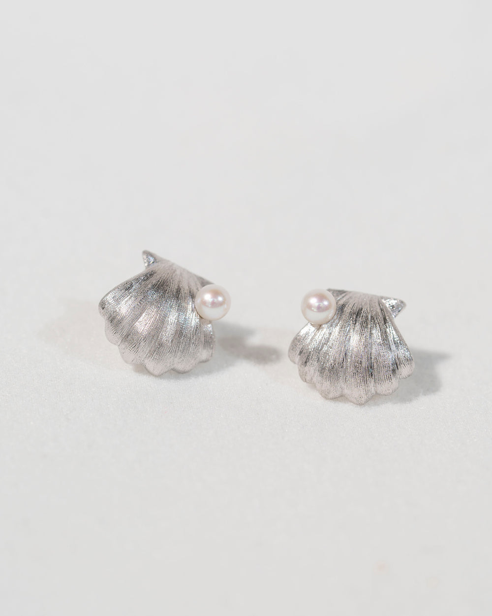 Pair of sterling silver shell stud earrings with freshwater pearls on a soft light background