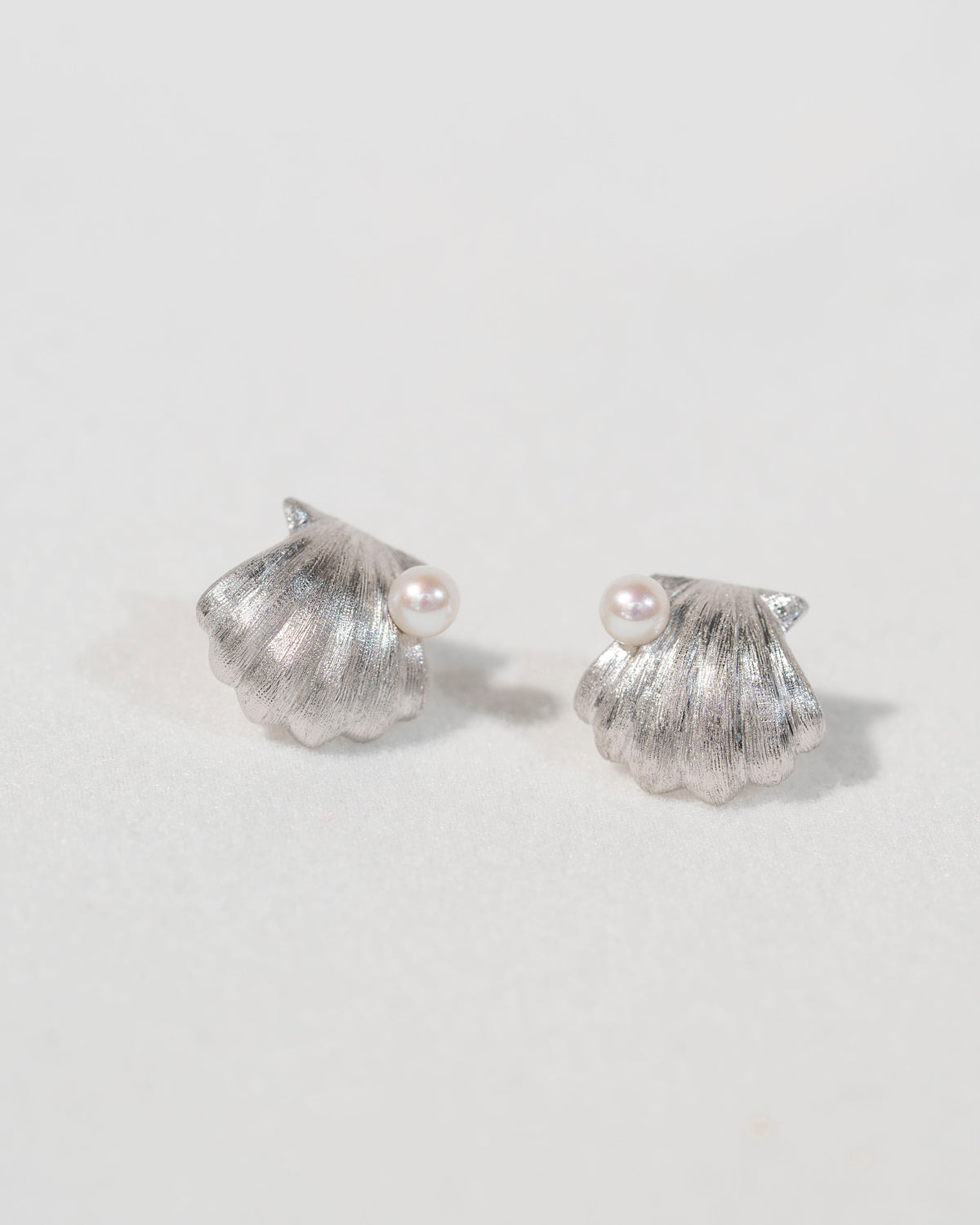 Pair of sterling silver shell stud earrings with freshwater pearls on a soft light background