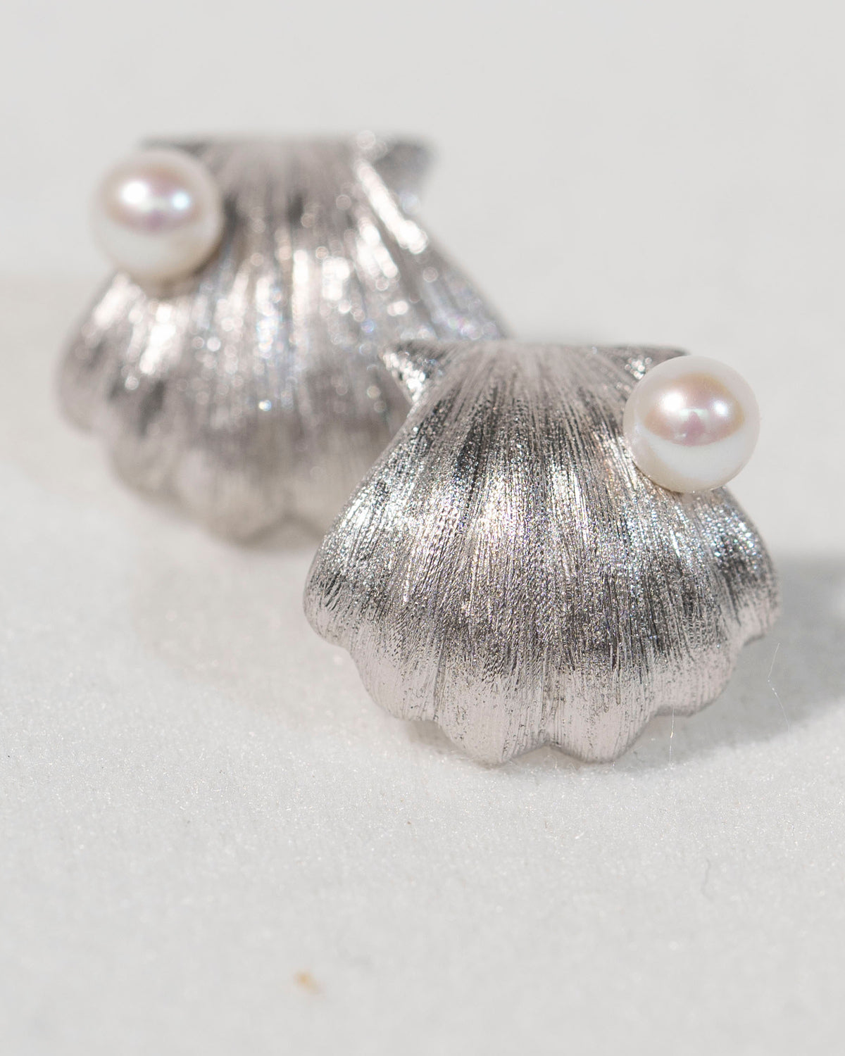 Close-up of sterling silver shell stud earrings with freshwater pearls showing hand-finished texture