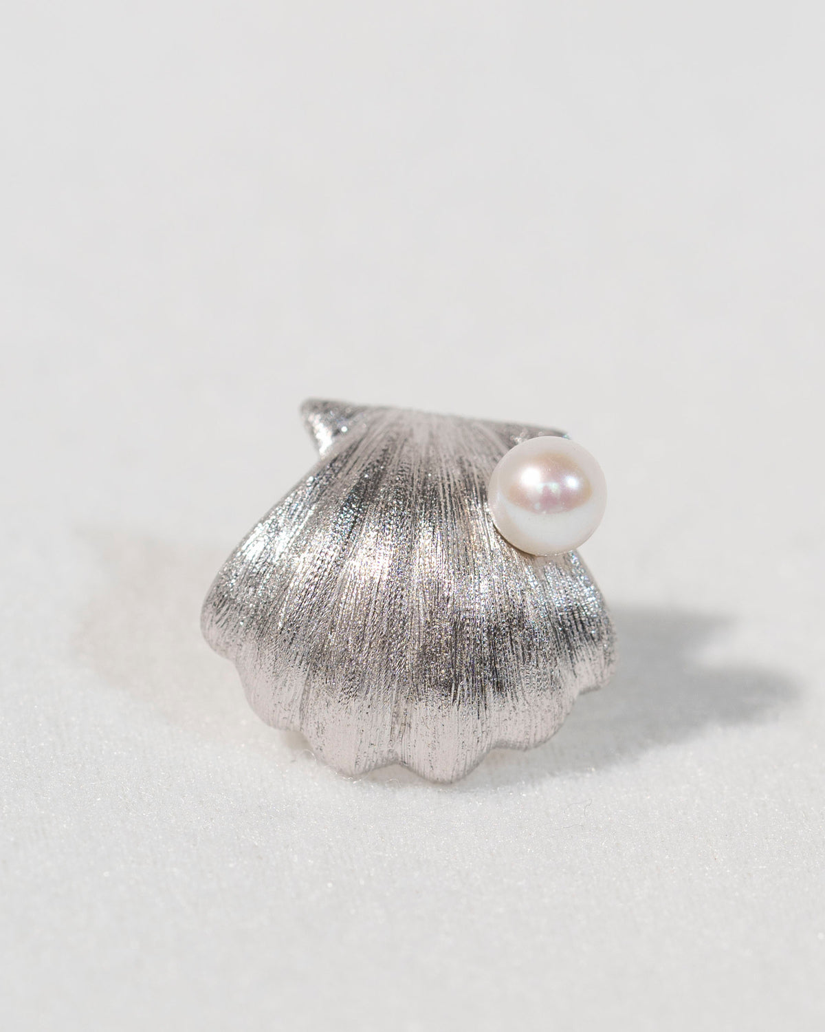 Single sterling silver shell stud earring with freshwater pearl on a light background