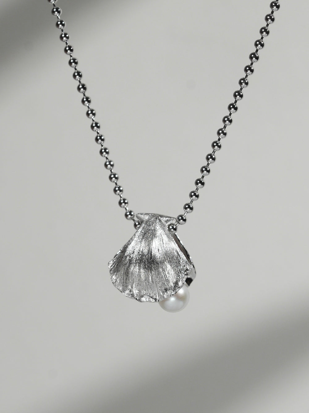 Close-up of shell pendant necklace with freshwater pearl on a soft gray background