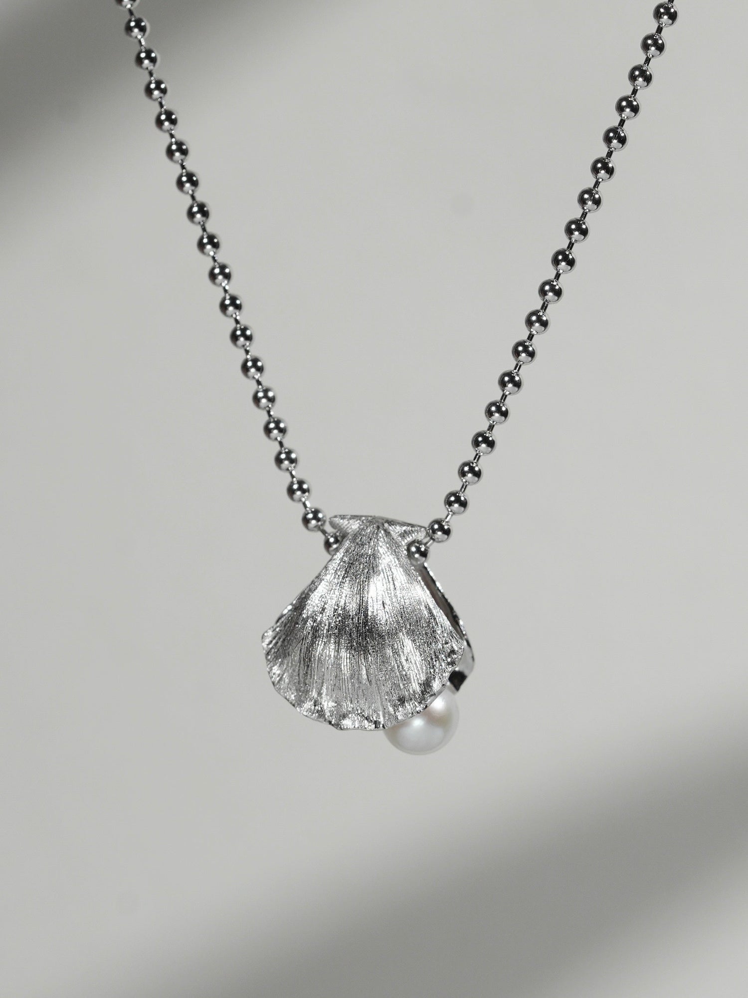 Close-up of shell pendant necklace with freshwater pearl on a soft gray background
