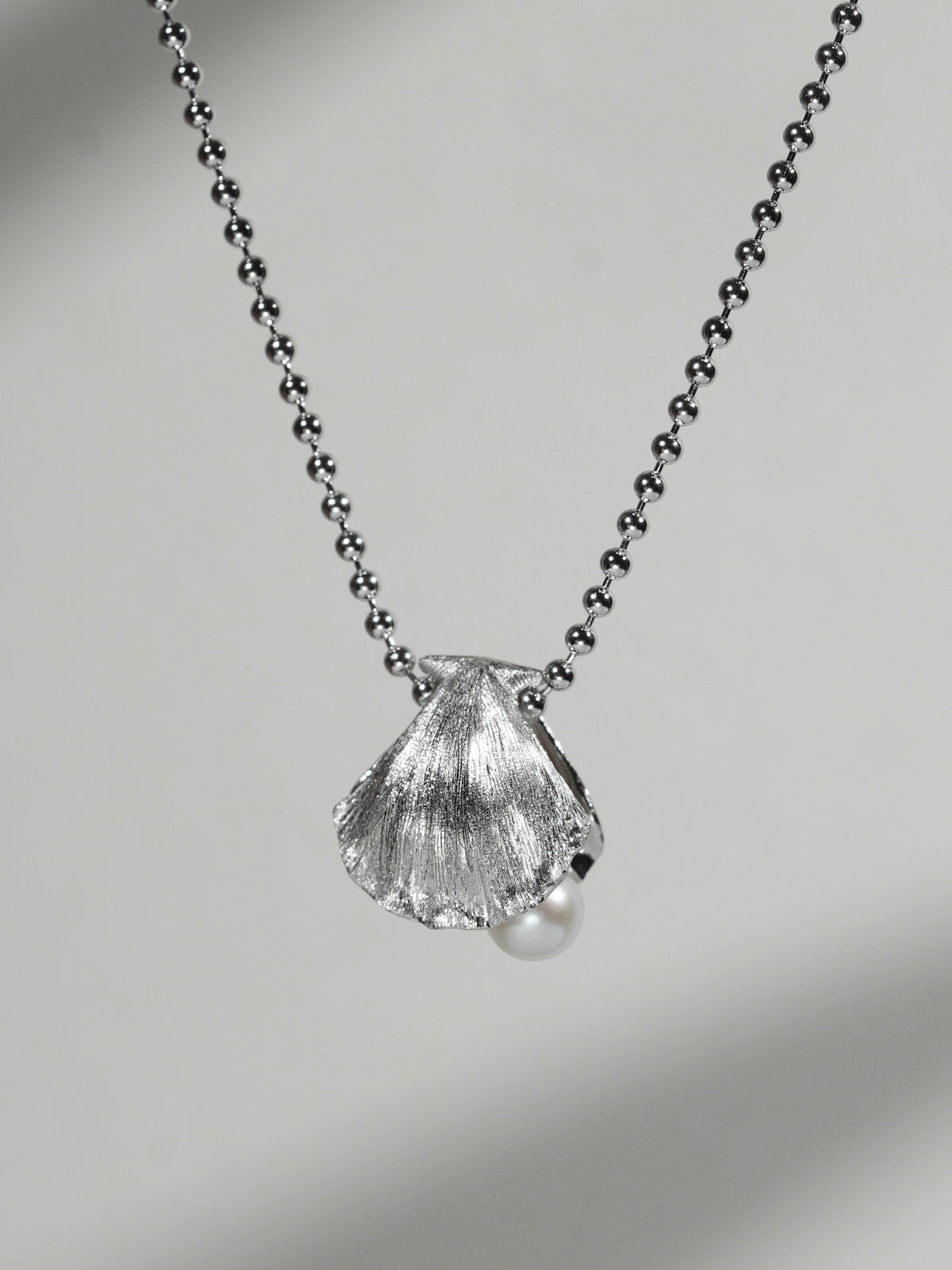 Close-up of shell pendant necklace with freshwater pearl on a soft gray background