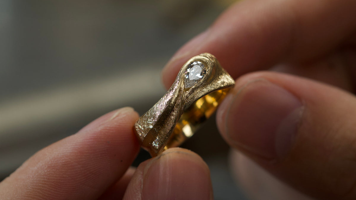 Close-up of a textured custom ring with a pear-shaped center stone.
