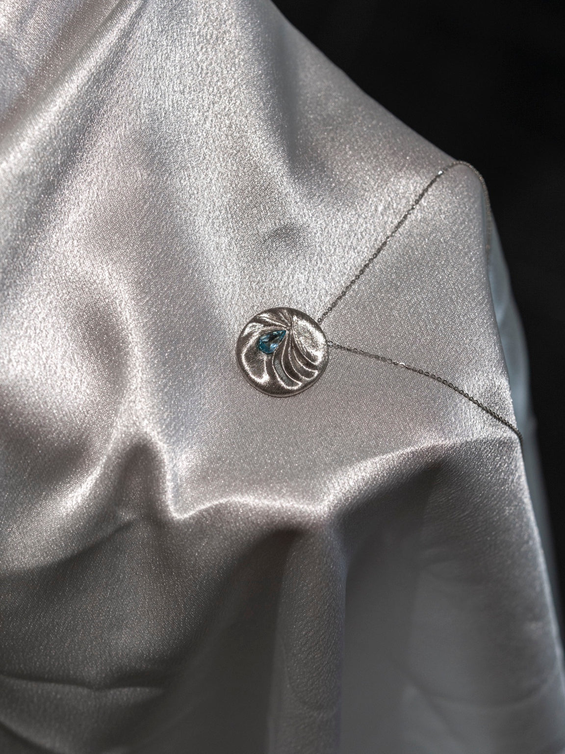 LIN 14k white gold pendant on folded silk, showing hand-textured folds following the outline of a pear-shaped aquamarine.