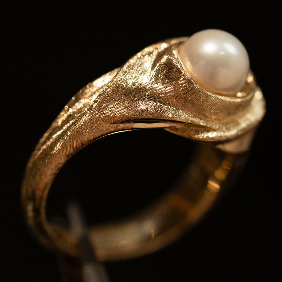 Close-up of the actual hand-worked silk texture on the 18K gold pearl ring, photographed against a dark background.