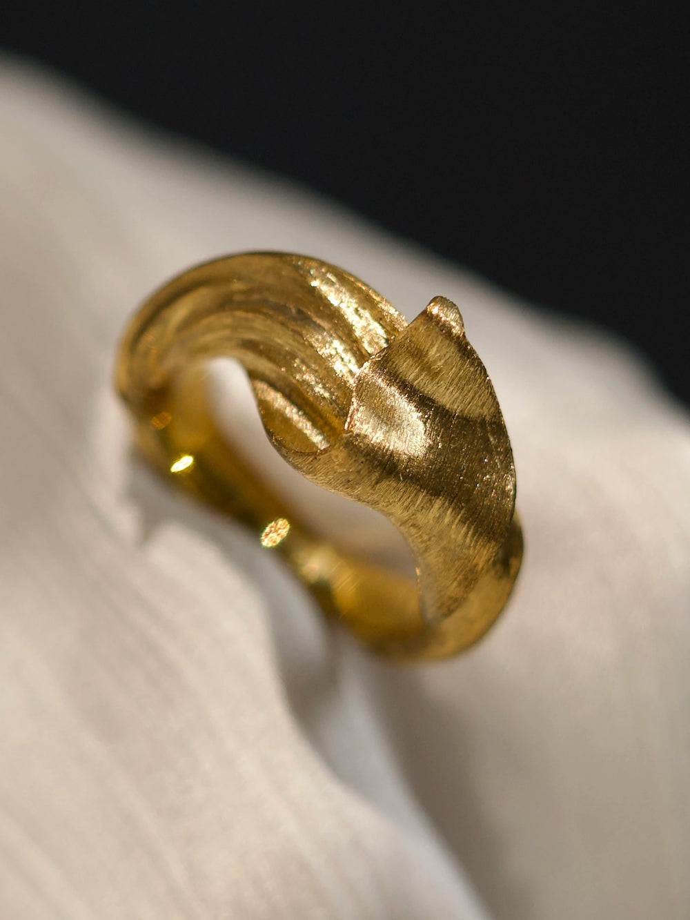 Solid 18K yellow gold Silk in Gold ring on pale fabric, showing sculptural folds and fine hand-worked texture.