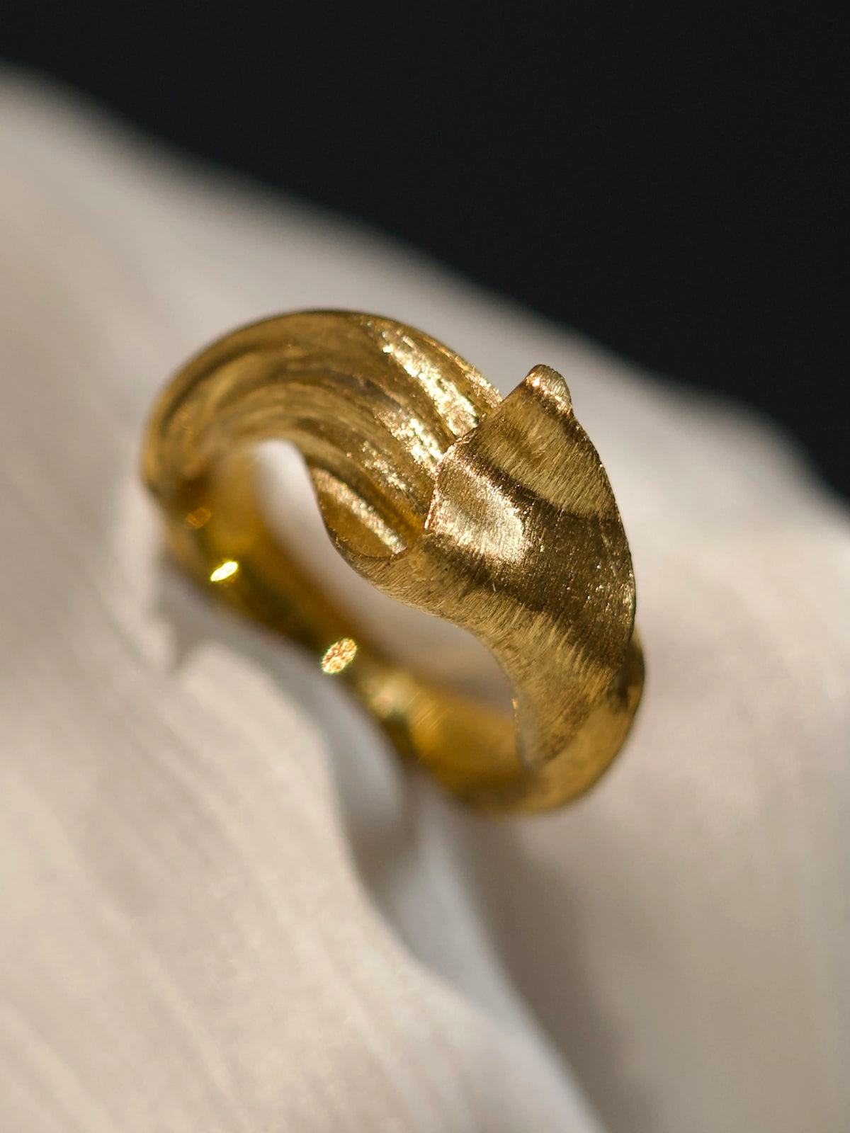 Solid 18K yellow gold Silk in Gold ring on pale fabric, showing sculptural folds and fine hand-worked texture.