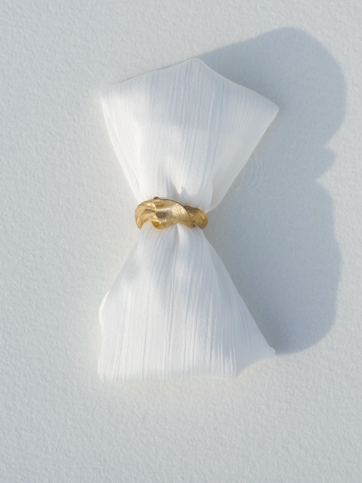 Silk in Gold ring gathering white folded fabric in sunlight, expressing the silk-inspired design.