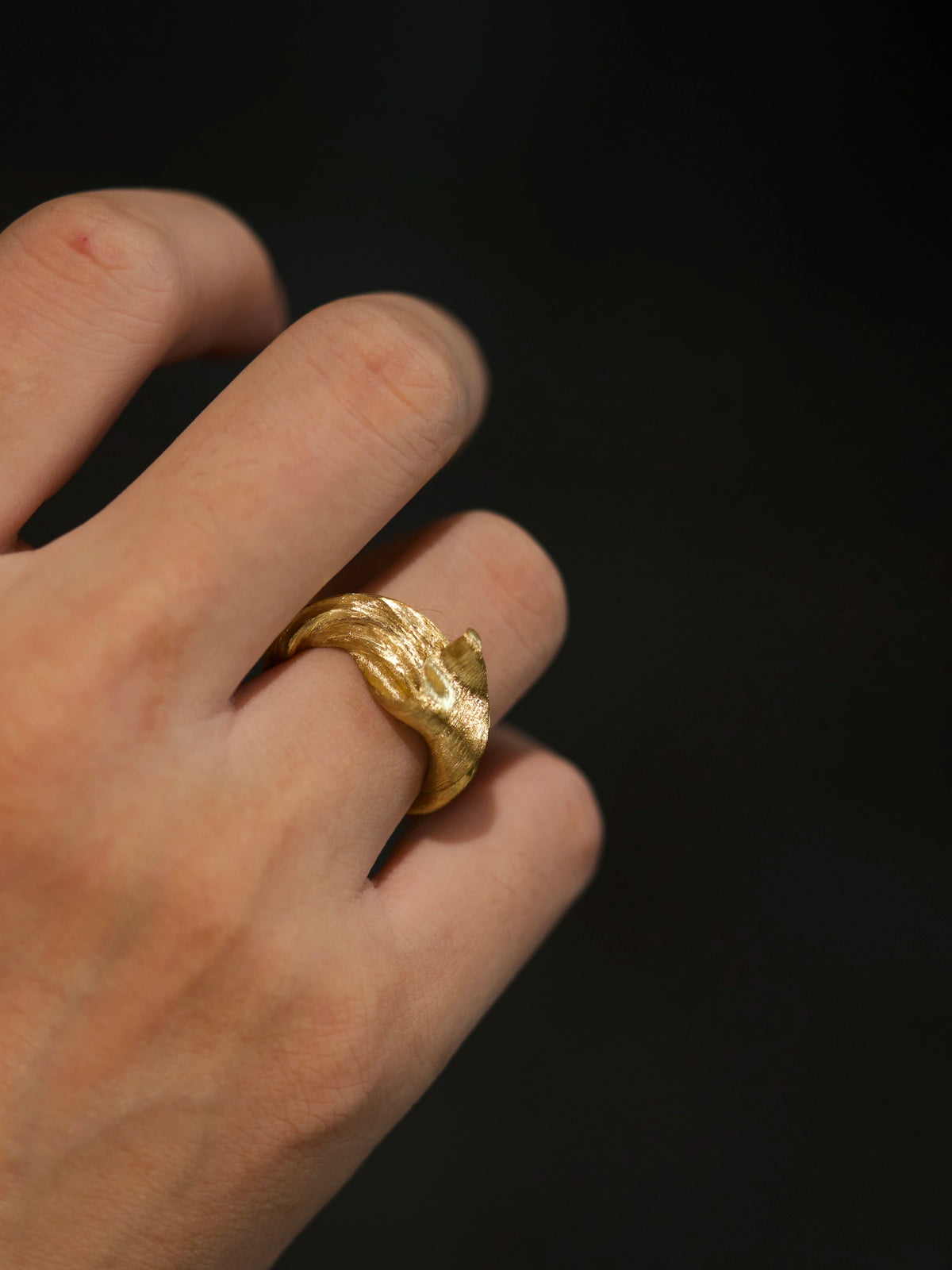 Silk in Gold sculptural ring worn on a hand, showing its scale and flowing gold folds.